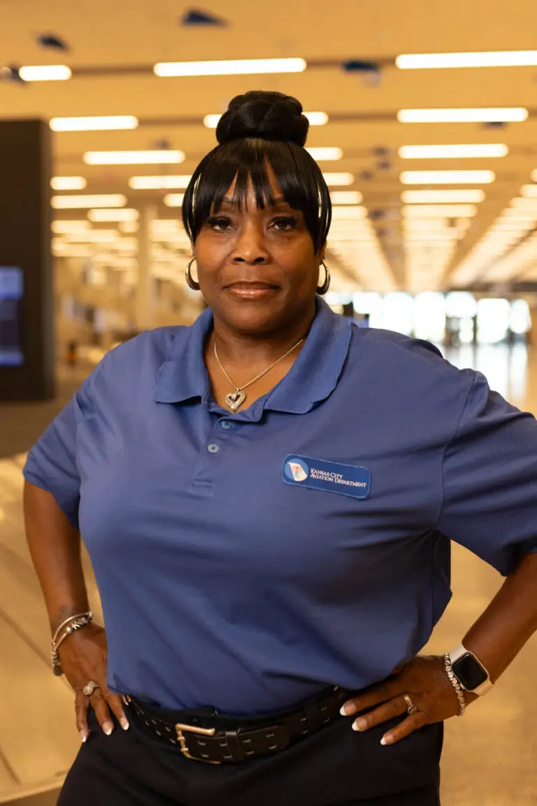 A woman in a blue Kansas City Aviation Department polo shirt stands with hands on hips